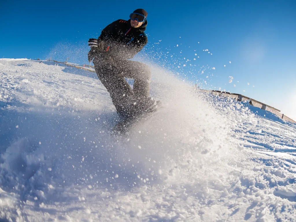 Ein Mann fährt an einem sonnigen Wintertag dynamisch Snowboard auf einer frisch beschneiten Piste.